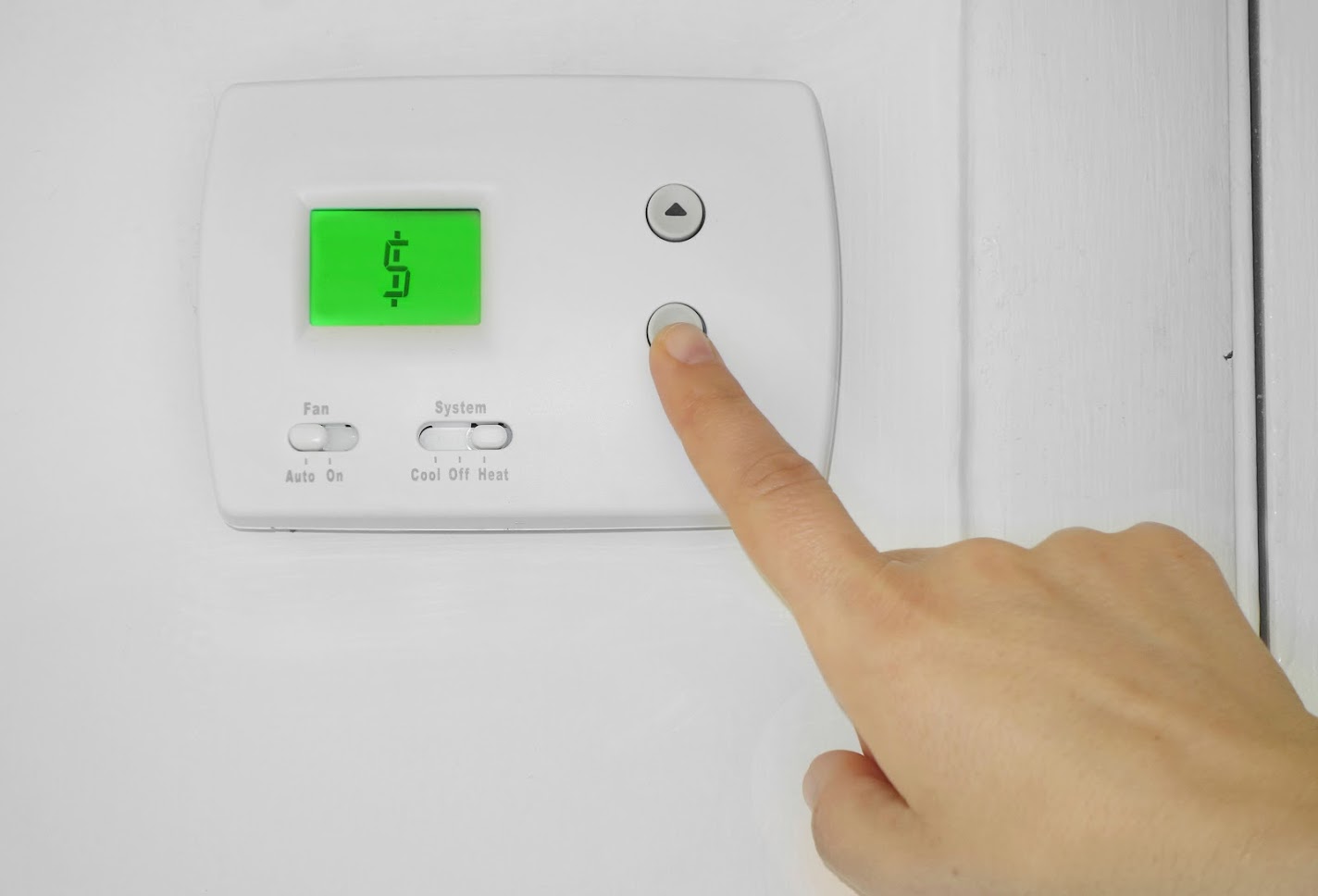 A person pushing the down arrow on a white thermostat 